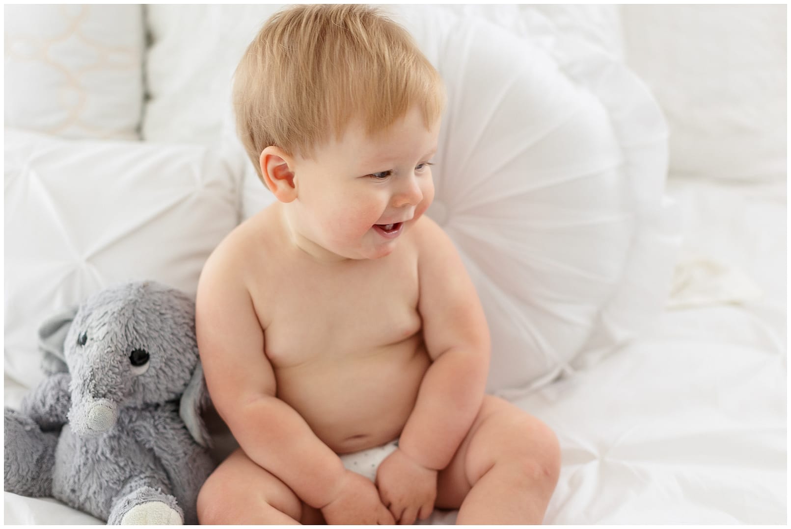 Baby in diaper smiles next to his stuffed elephant. Photo by Tiffany Hix Photography.