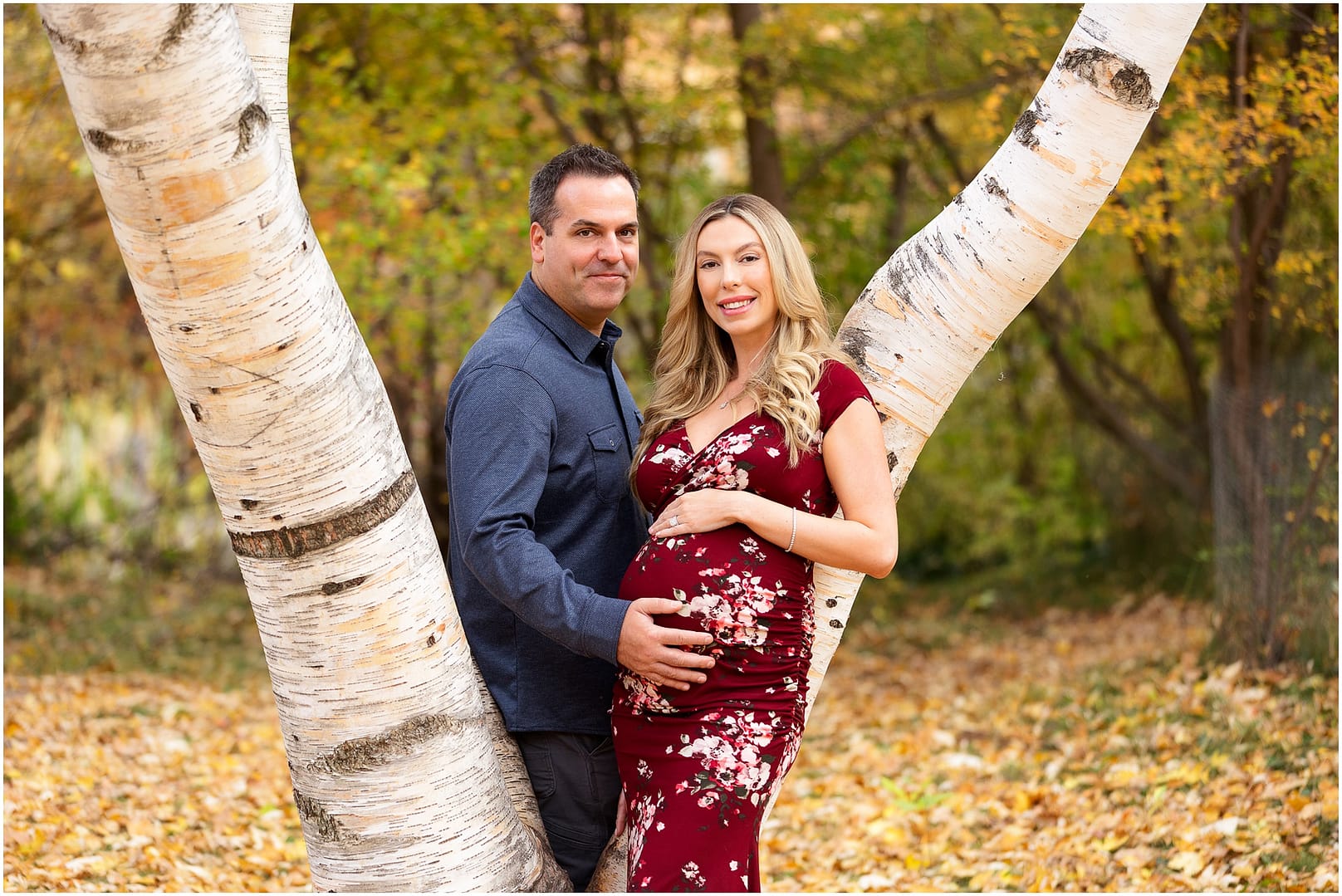 Dad places his hand on wife's baby bump while standing in front of a tree. Photo by Tiffany Hix Photography.