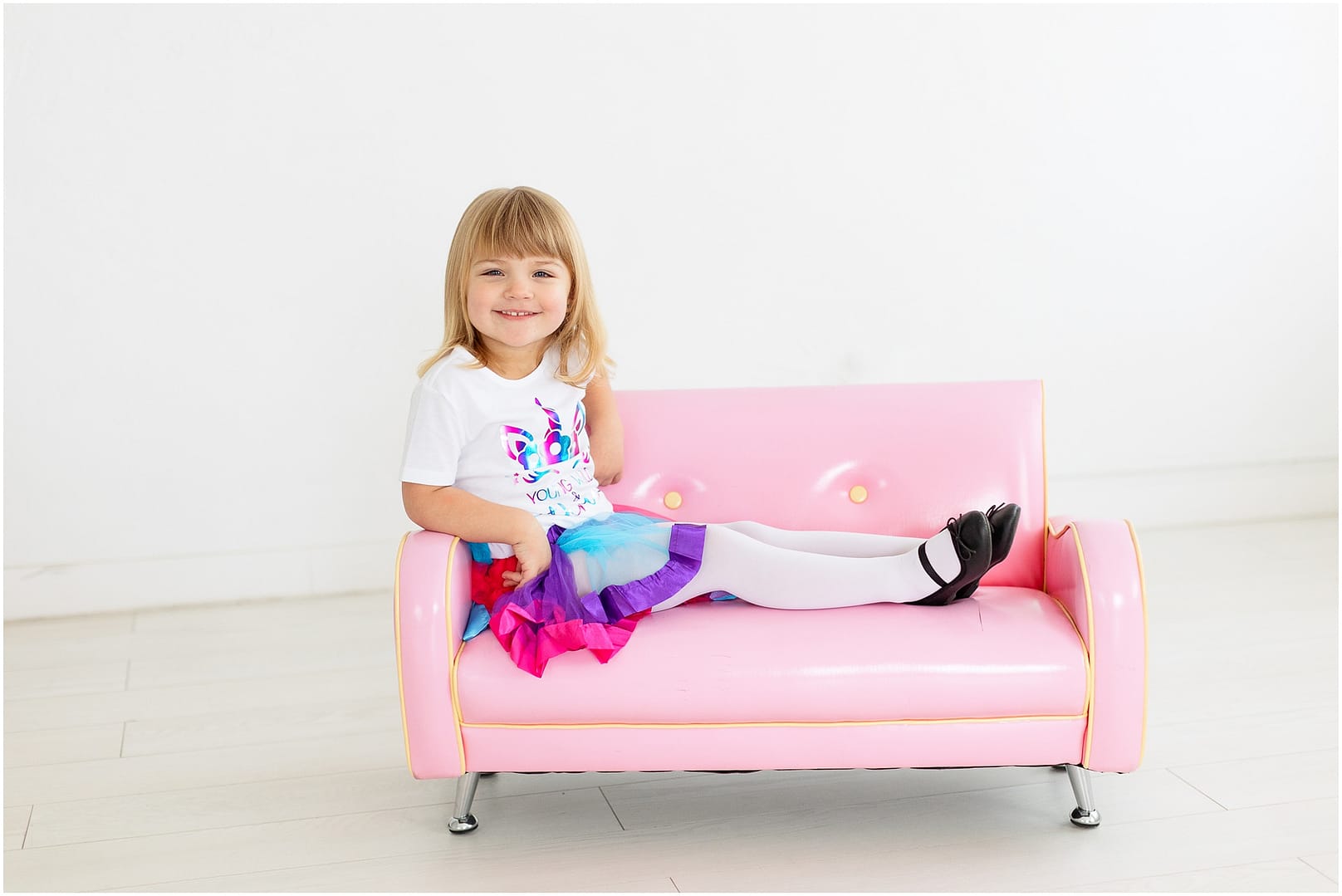 Little girl sits on pink couch in her unicorn outfit. Photo by Tiffany Hix Photography.