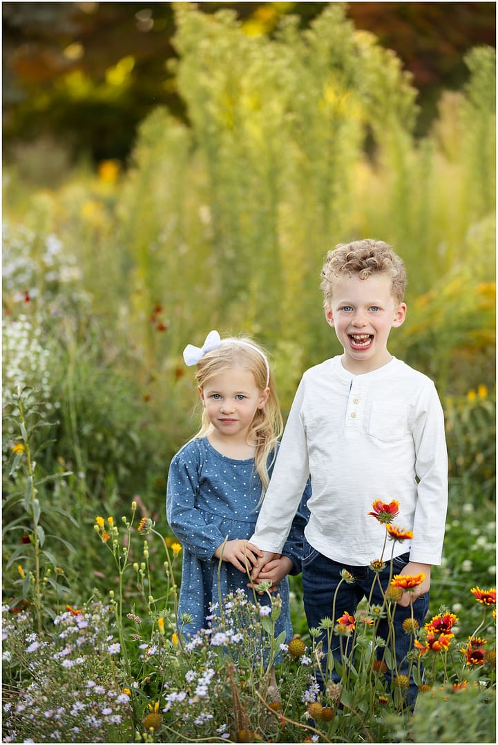 Brother and sister hold hands among the wildflowers. Photo by Tiffany Hix Photography.