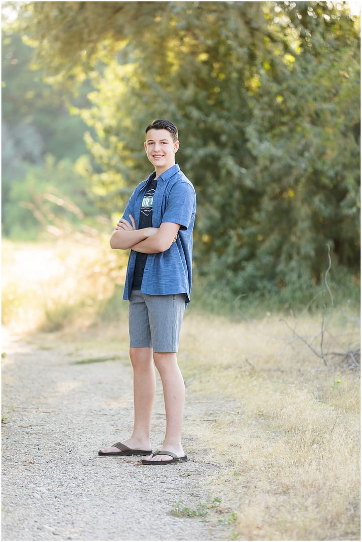 Teen boy stands with his arms crossed on gravel pathway. Photo by Tiffany Hix Photography.