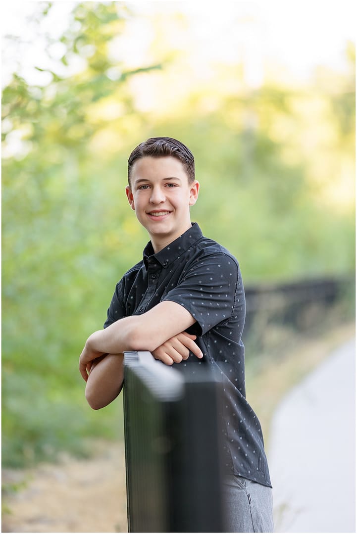 Teen boy in black shirt leans against fence during Boise portrait session. Photo by Tiffany Hix Photography.