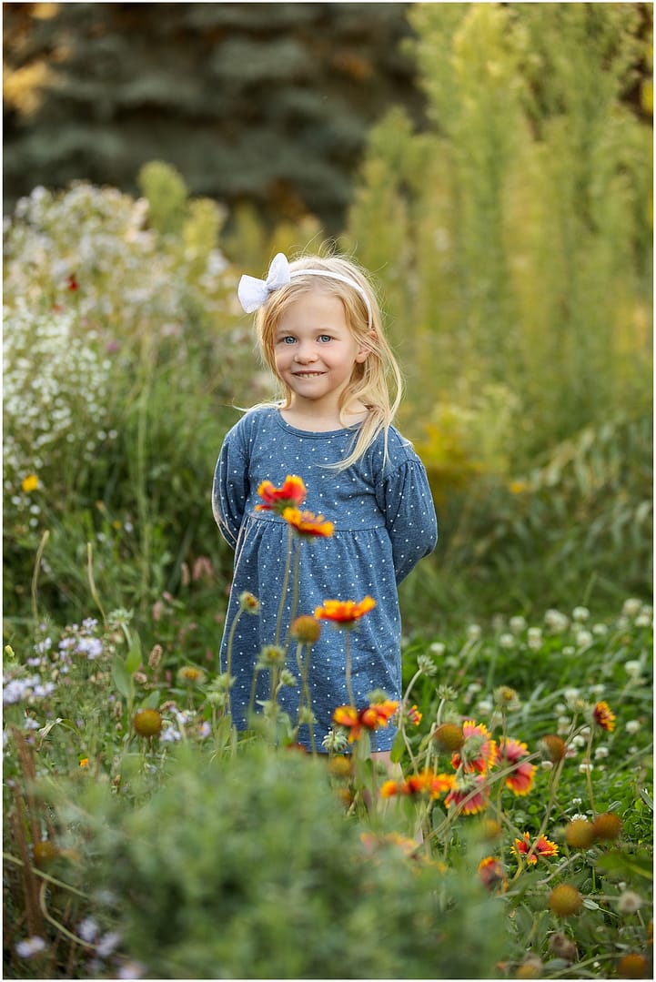 Little girl smiles coyly among the wildflowers. Photo by Tiffany Hix Photography.