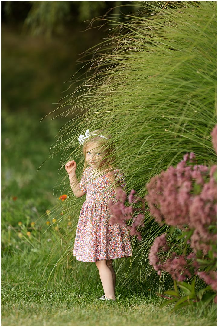 Little girl plays peek-a-boo behind tall grasses. Photo by Tiffany Hix Photography.