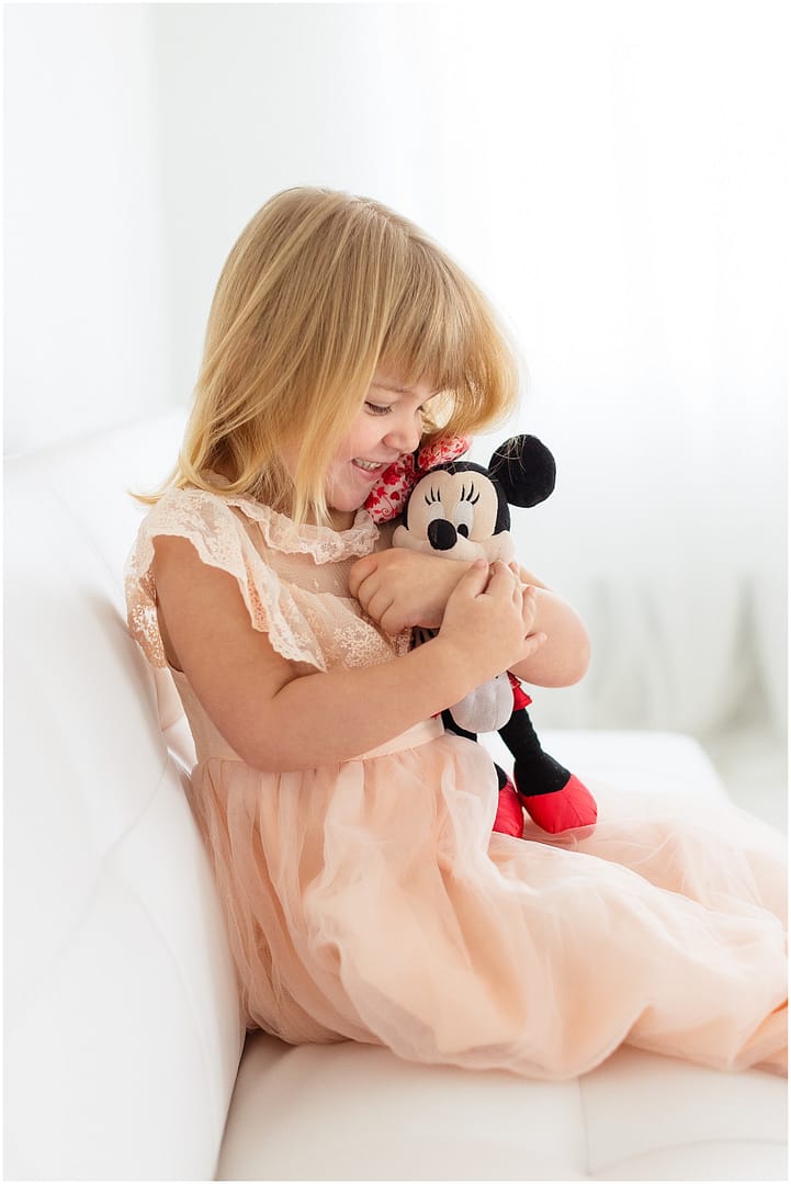 Little girl giggles while clutching Minnie Mouse plush. Photo by Tiffany Hix Photography.