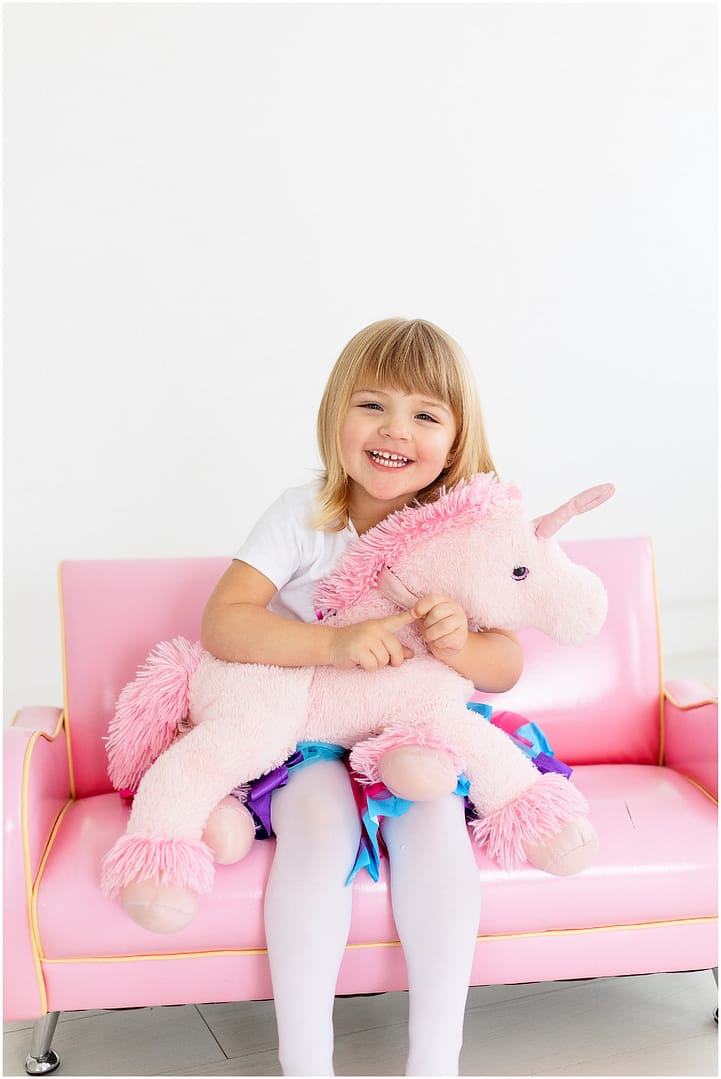 All smiles while holding a large pink stuffed unicorn. Photo by Tiffany Hix Photography.