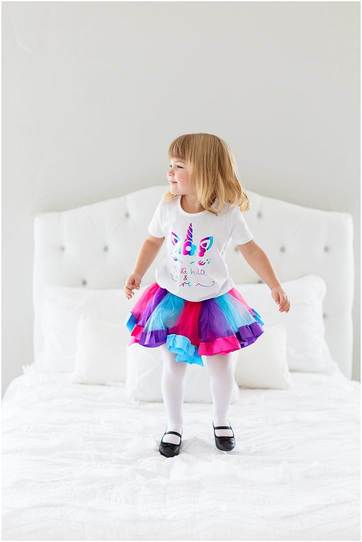 Little girl jumps on bed in unicorn birthday outfit. Photo by Tiffany Hix Photography.