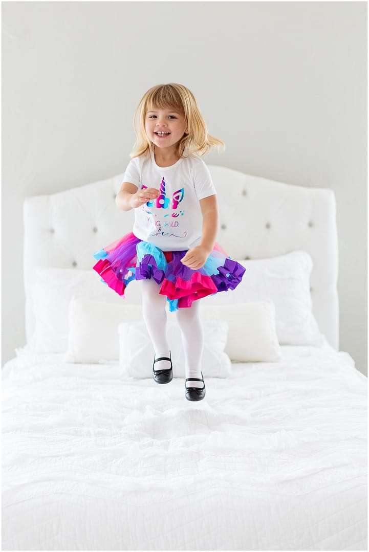 Little girl jumps on bed during birthday photo session. Photo by Tiffany Hix Photography.