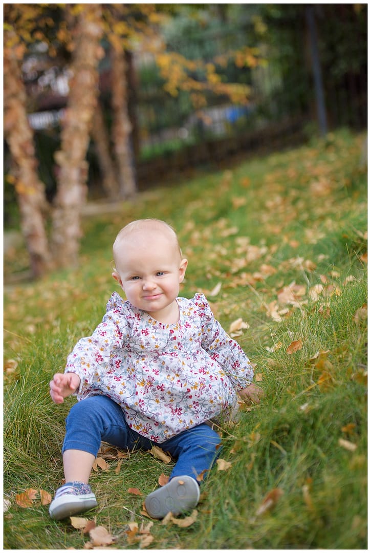 Baby girl scrunches nose while sitting on grass. Photo by Tiffany Hix Photography
