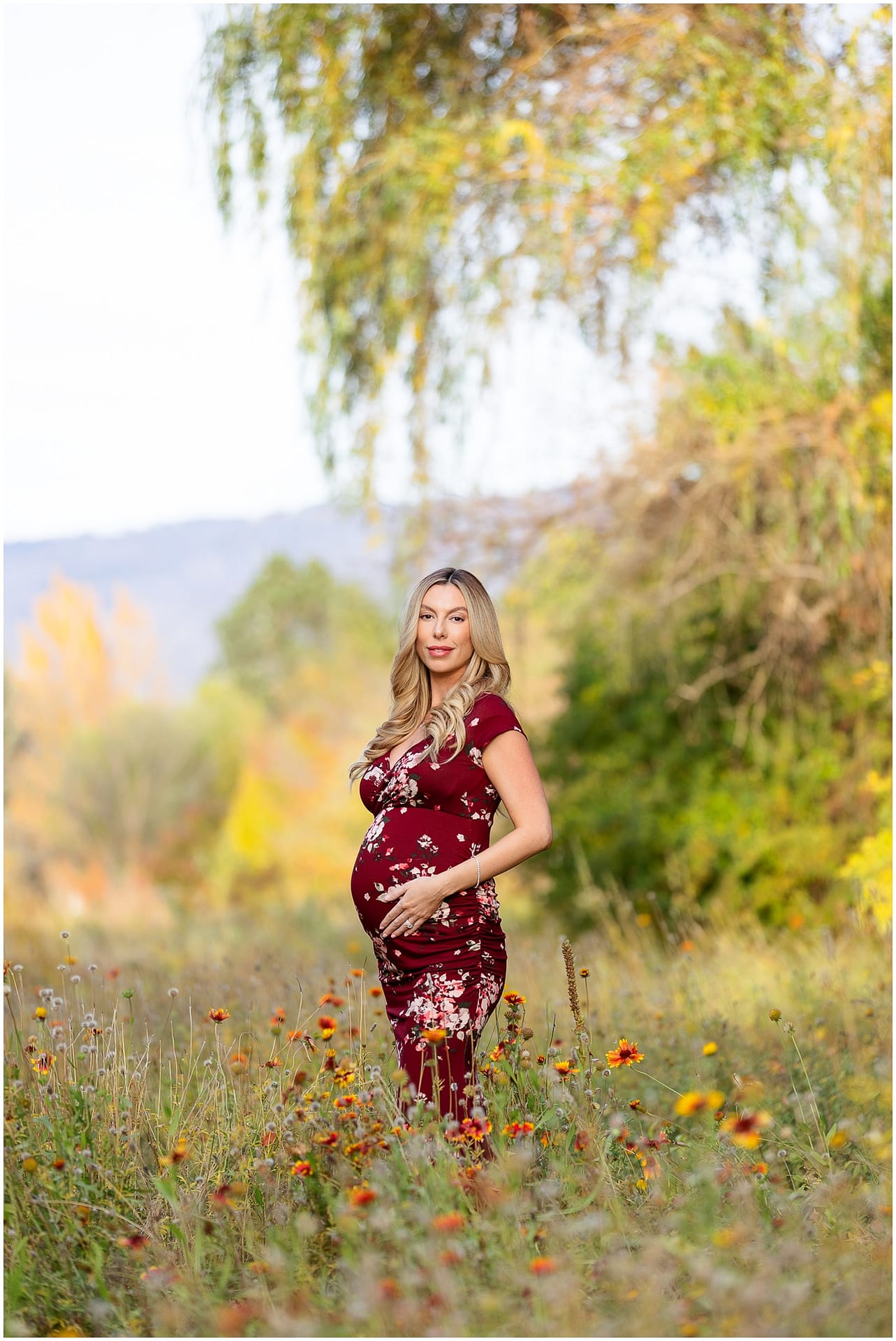 Mom stands in field of wildflowers cradling baby bump. Photo by Tiffany Hix Photography.